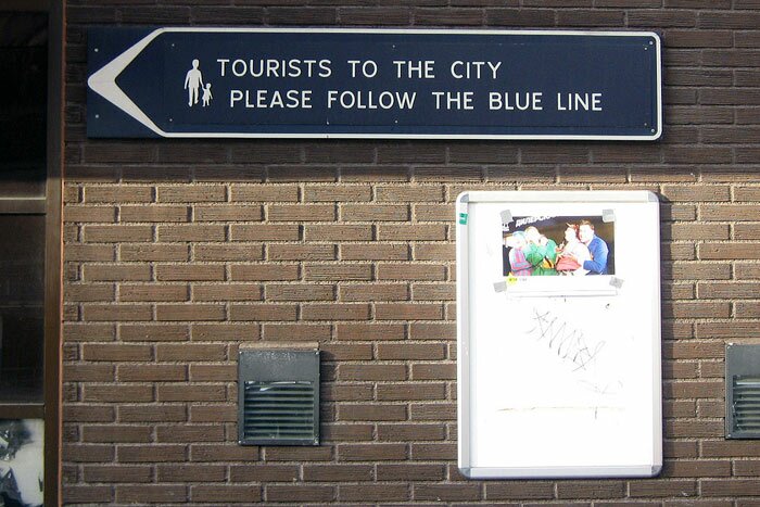 Табличка: Tourists to the city please follow the blue line